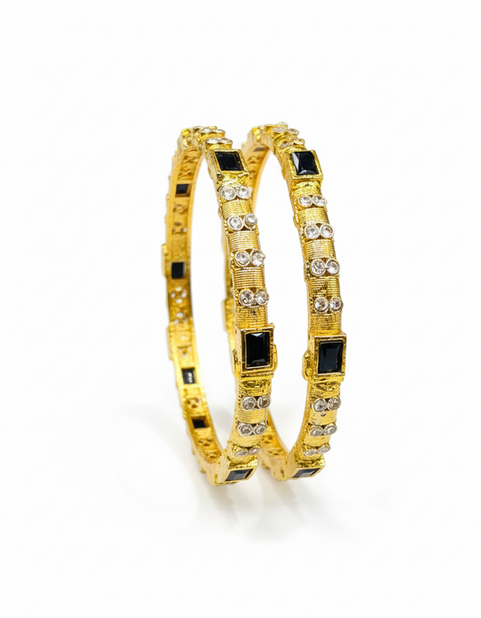 Gold bangles with black stones and clear stones on a white background